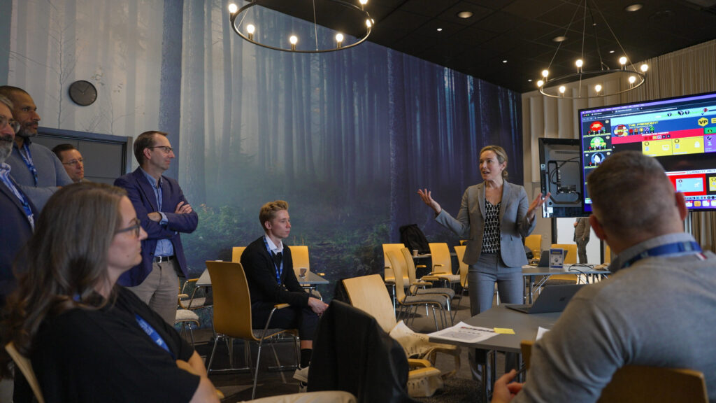 A woman standing in front of a group of people, speaking and gesturing.