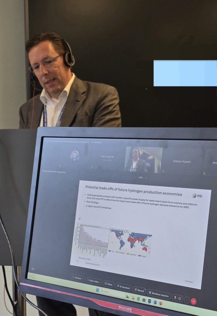 A man with a headset standing behind a computer screen.